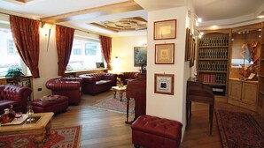 A traditional living room with leather sofas, a wooden coffee table, and a bookshelf filled with books and decorative items. - Hotel Bes & Spa (Claviere)