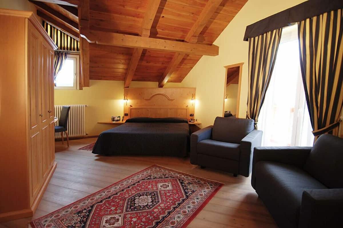 A bedroom with a wooden ceiling, a bed, a sofa, a chair, and a large window with curtains.