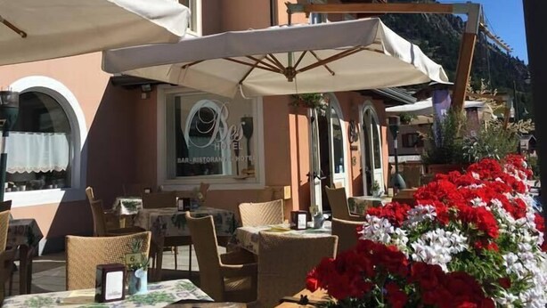 An outdoor seating area with tables and chairs, a sign for 'Hotel B', and a balcony with a wooden railing. - Hotel Bes & Spa (Claviere)