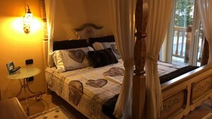 A bedroom with a four-poster bed, heart-shaped pillows, a bedside table, and a lamp. - Hotel Bes & Spa (Claviere)