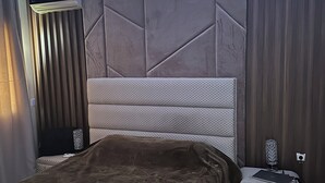 A modern bedroom with a large bed, a bedside table, a lamp, and a wall-mounted speaker. - High standing apartment PERLA SAIDIA 3min walk from the beach (Saïdia)