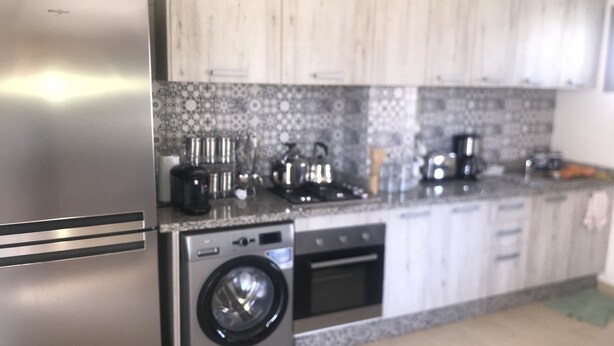 A kitchen with a stainless steel refrigerator, a washing machine, a coffee maker, and a toaster.