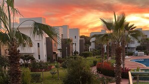 A resort with modern buildings, a pool, and a well-maintained garden with palm trees and shrubs.