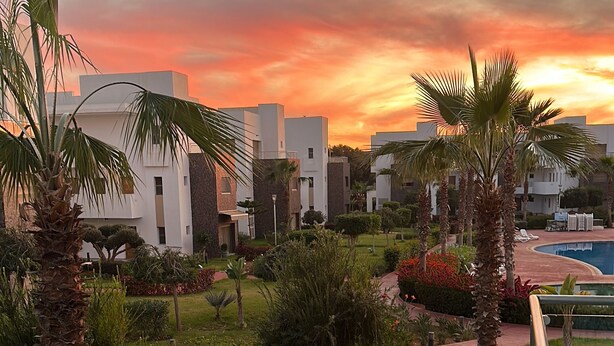 A resort with modern buildings, a pool, and a well-maintained garden with palm trees and shrubs. - High standing apartment PERLA SAIDIA 3min walk from the beach (Saïdia)