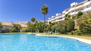 Una piscina con lettini, circondata da verdeggiante vegetazione e edifici bianchi.