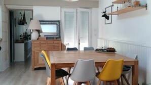Ein Essbereich mit einem Holztisch und Stühlen, einem Fernseher und einer Küche im Hintergrund.