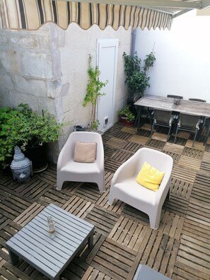 An outdoor patio with a wooden table, two white plastic chairs, a small table, and potted plants. - Ideal for your spa treatment or summer or winter vacation.  (Rochefort)