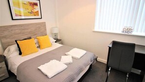 A hotel room with a bed, two pillows, a desk, a chair, a lamp, and a window with blinds. - Overnight Stay Chester With Parking (Chester)