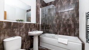 A modern bathroom with a toilet, pedestal sink, bathtub, and a glass-enclosed shower.