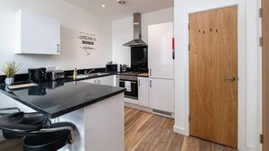 A modern kitchen with white cabinets, a black countertop, and a wooden door.