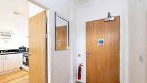 A hallway with a wooden door, a fire extinguisher, and a mirror on the wall.