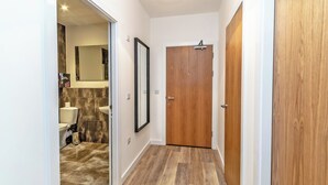 Un couloir avec une porte en bois, un miroir et une salle de bain comprenant des toilettes et un lavabo.