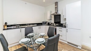 Une cuisine moderne avec des meubles blancs, un plan de travail noir et un coin repas comprenant une table et des chaises en verre.