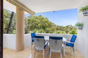 A patio with a table and chairs, a white wall, and a view of trees. - B07 Caserio - Apartment close to the beach (Sitio de Calahonda)