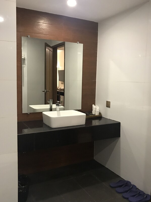 Une salle de bain moderne avec un grand miroir, un lavabo blanc et des carreaux de couleur foncée.