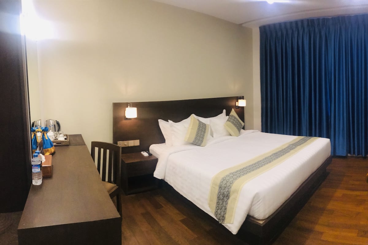 Habitación de hotel con una cama, un escritorio, una silla, una mesita de noche y un televisor montado en la pared.