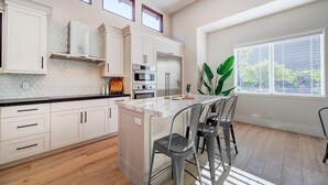 A modern kitchen with white cabinets, a marble countertop, and a central island with bar stools. - LaFave-Luxury Home at Zion: West Temple (Springdale)