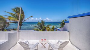 Un balcon avec deux chaises et une petite table, donnant sur une plage bordée de palmiers et sur l’océan.