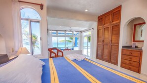 Une chambre d’hôtel avec un grand lit, une armoire en bois, un bureau avec une chaise et une vue sur l’océan.