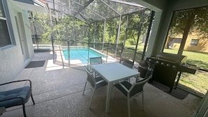 Ein überdachter Patio mit Pool, Tisch, Stühlen und Grill.