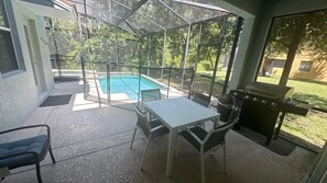 A screened-in patio with a pool, a table and chairs, and a grill. - Private Pool & Spa | Private Backyard | BBQ Included | Game Room | 5BR Near Disney (Kissimmee)