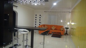 A modern living room with a dining area, featuring a sofa, a table, and bar stools.