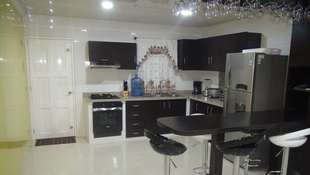 A modern kitchen with dark cabinets, a central island with bar stools, a refrigerator, and a microwave.