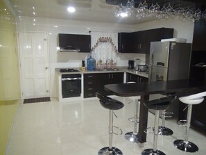 A modern kitchen with dark cabinets, a central island with bar stools, a refrigerator, and a microwave. - Vacation home in San Andrs for up to 14 (San Andrés Islas)