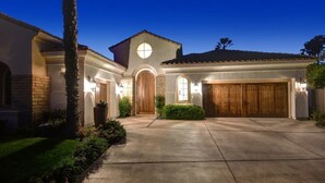 Une maison d’habitation avec une entrée centrale en arc de cercle, une grande porte de garage en bois et une allée bien éclairée.