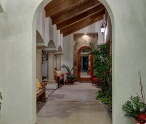Stroll through this elegant corridor, lined with arches and potted plants, leading to a stone door with a wooden frame.