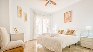 Quarto com cama, mesa de cabeceira, cadeira e ventilador de teto.