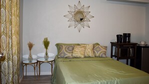 Una habitación con una cama, un espejo redondo, una mesita con dos jarrones y una cafetera.