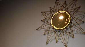 Una habitación con decoración de pared en forma de estrella, una cama con almohadas estampadas y un jarrón con plantas secas.
