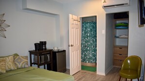 Habitación compacta con cama, un escritorio pequeño con cafetera, armario y una silla verde.