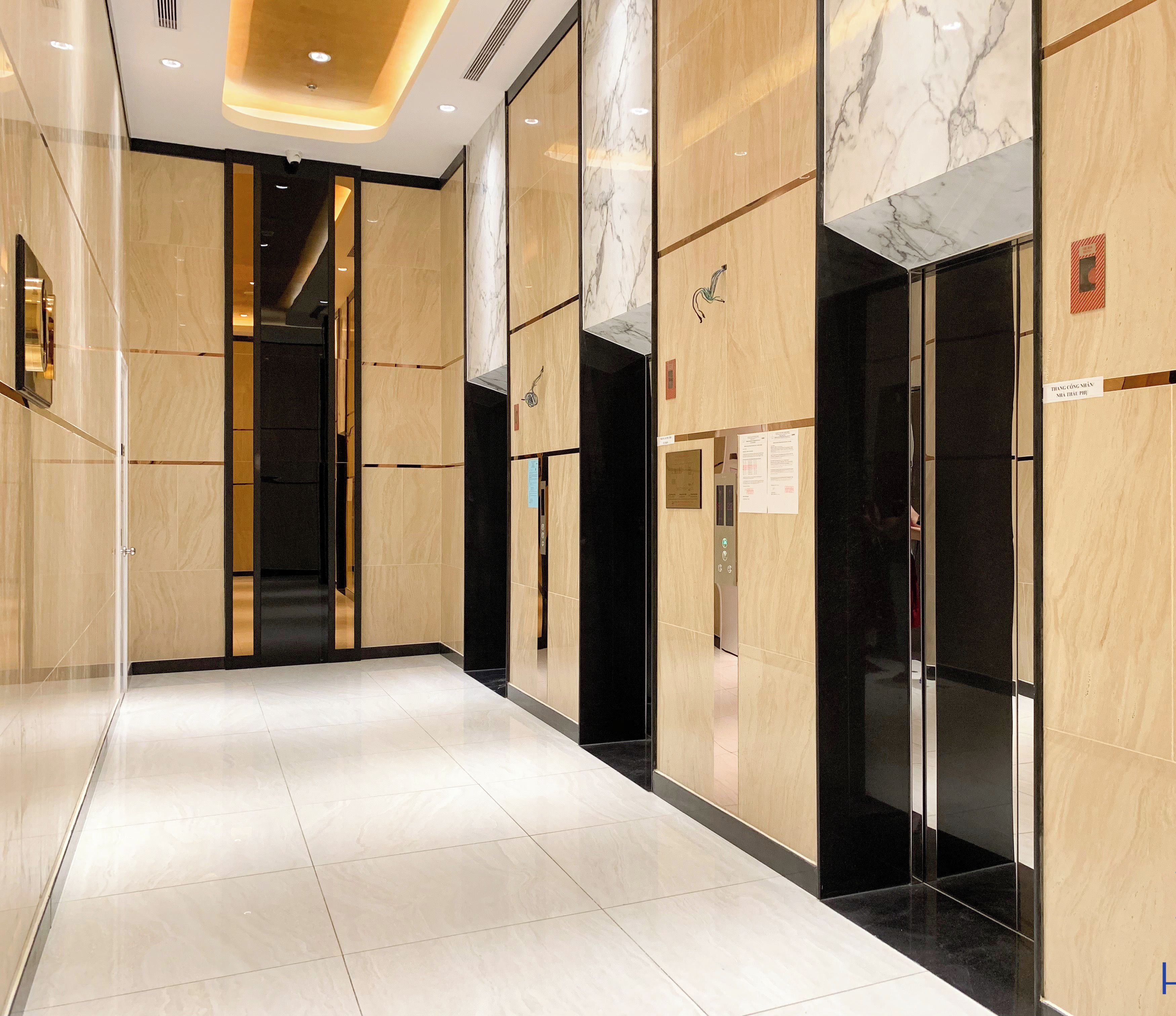 A modern hotel corridor with marble walls, a tiled floor, and an elevator.