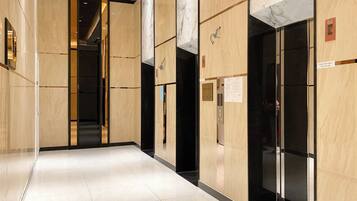 A modern hotel corridor with marble walls, a tiled floor, and an elevator.