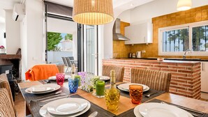 A dining area with a brick kitchen, wicker chairs, and a table set for four. - J03 Villa Mabola - Villa (Sitio de Calahonda)
