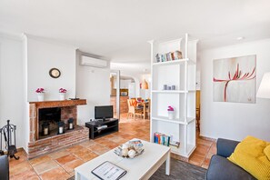 Una sala de estar con chimenea, televisor, estantería y un cuadro en la pared.