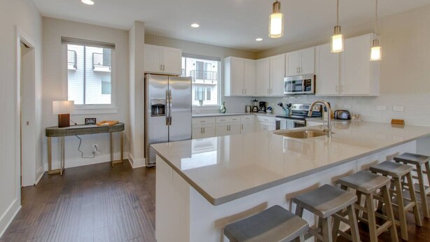 A modern kitchen with white cabinetry, stainless steel appliances, a large island with bar stools, and pendant lighting.
