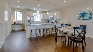 A modern kitchen with white cabinets, a central island, bar stools, and pendant lighting.