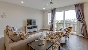 A living room with a sofa, a coffee table, a TV on a stand, and a balcony with curtains.