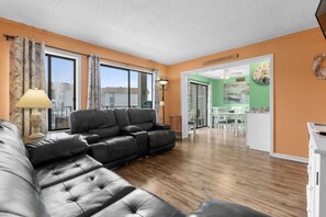 A living room with a black leather sofa, a lamp, and a dining area with white chairs and a table. - A448 at The Myrtle Beach Resort (Myrtle Beach)