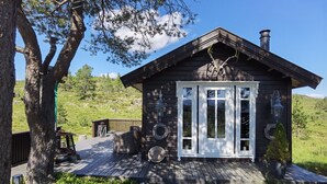 A wooden cabin with a deck, large windows, and a chimney. - High standard cabin with view, hiking and fishing Ocean boat rental possible (Raudsand)