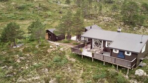 A two-story cabin with a deck, surrounded by a forested landscape. - High standard cabin with view, hiking and fishing Ocean boat rental possible (Raudsand)