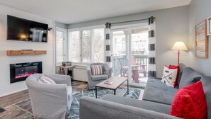 Una sala de estar moderna con chimenea, sofás grises, una mesa de centro y un televisor montado en la pared.