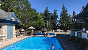 Una piscina con una silla de salvavidas, sillones de descanso y un pequeño edificio con una puerta azul.