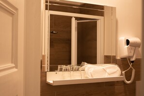 Une salle de bain équipée d’un miroir, d’un porte-serviettes et d’un sèche-cheveux fixé au mur.