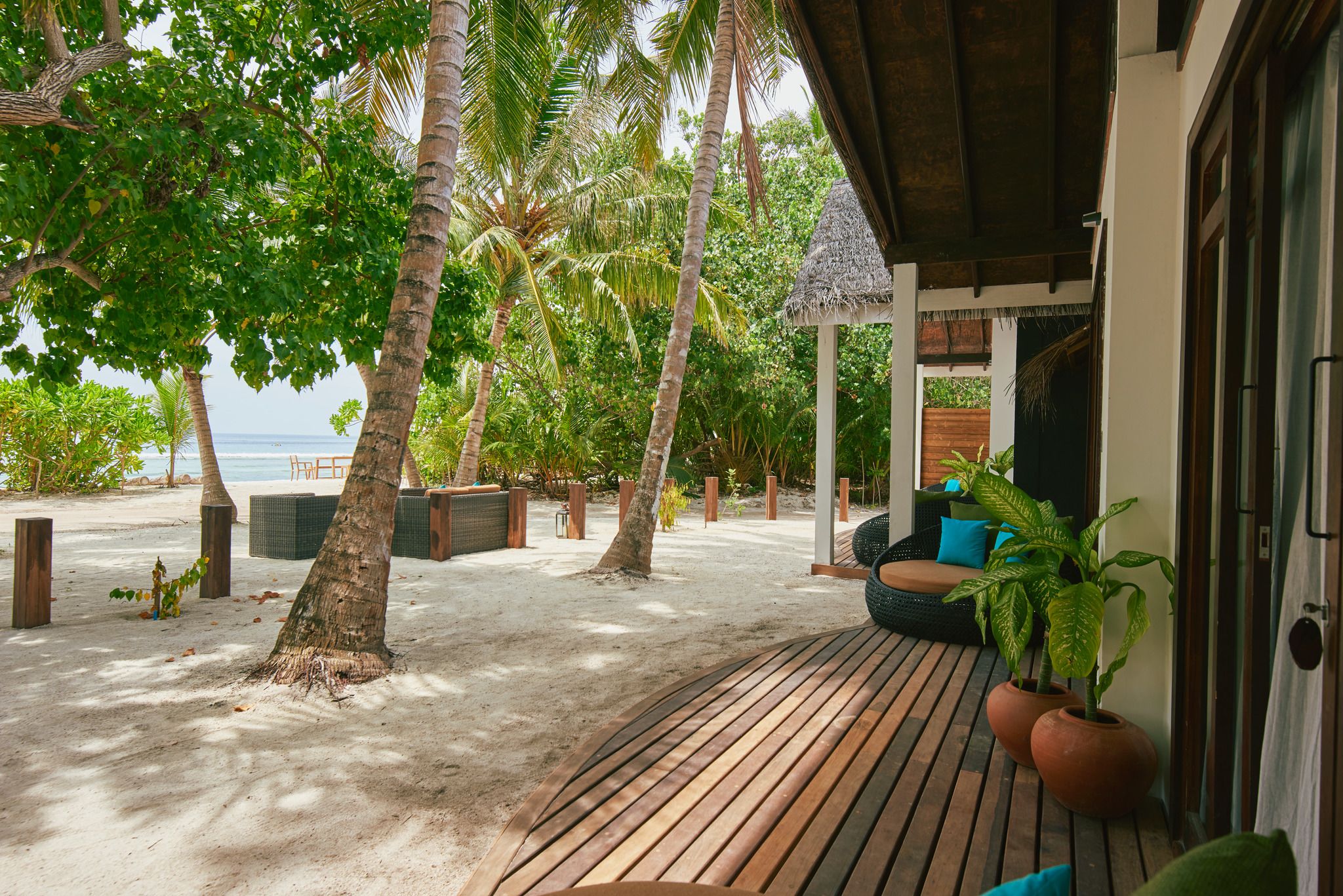 A wooden deck with a seating area, surrounded by palm trees and a view of the sea.