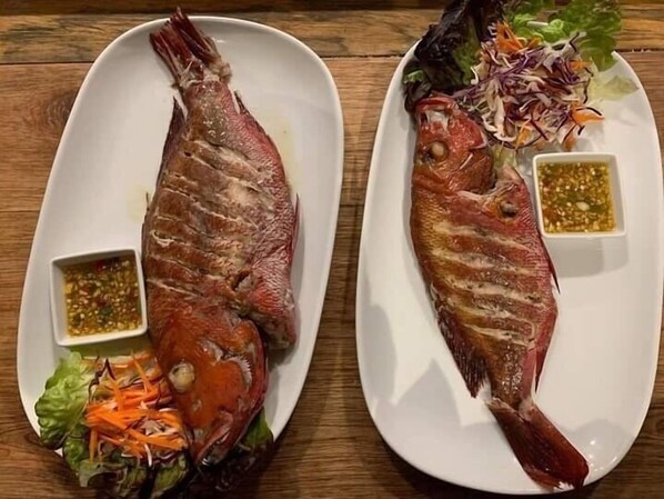 Two plates of grilled fish with side salads and dipping sauces.