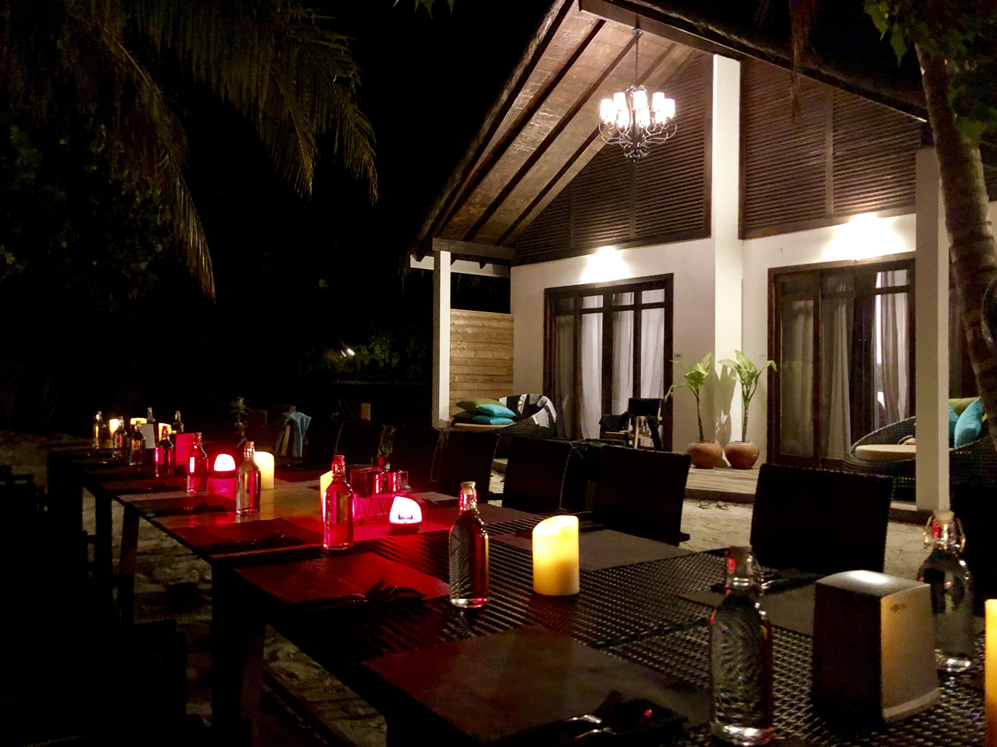 An outdoor dining area with tables set for a meal, candles, and a chandelier.